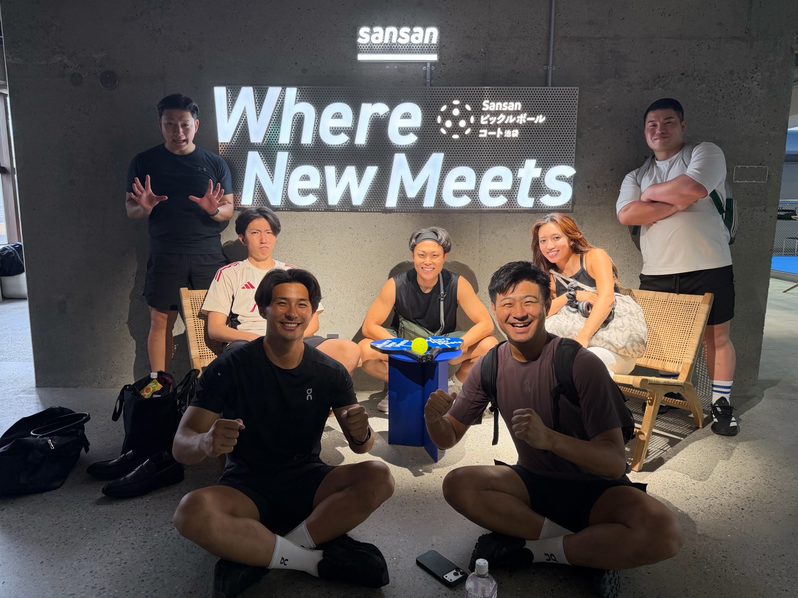 ピックルボールコートの「Where New Meets」の看板前で集合するメンバーたち